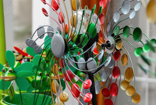 Colorful decorative wind spinner with metallic blades and vibrant accents, surrounded by playful garden ornaments in a bright outdoor setting