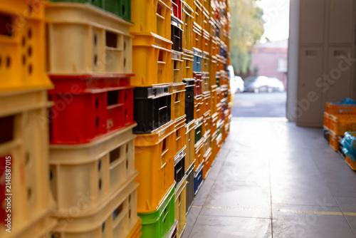 rows of stacked plastic crates in yellow, red, black, green, and beige line warehouse aisle, with shallow depth of field, soft light, and storage order, with crate