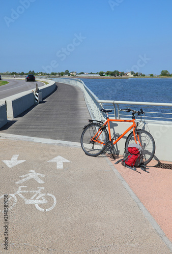 Canvastavla Orange bicycle and red backpack parked along scenic coastal cycle path on sunny