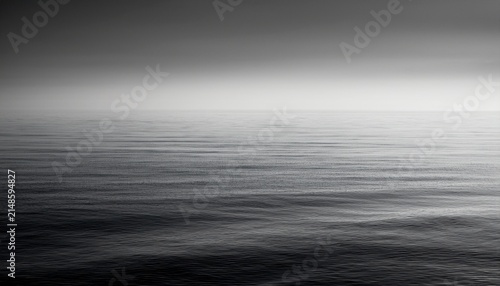 A Black And White Photo Of A Calm Ocean With Fog In The Distance