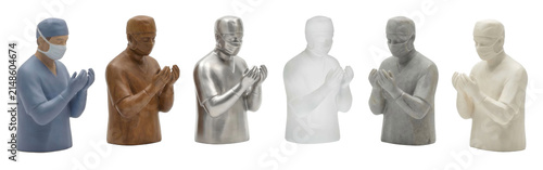 Six statuettes of a praying surgeon in scrubs and a face mask stand in a row, each figure crafted from a unique material including wood, metal, stone, and glass