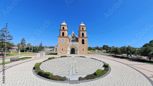 View of St Francis Xavier's Cathedral with its distinctive twin towers and stone facade, set behind a circular stone labyrinth in Geraldton, Western Australia, Australia.