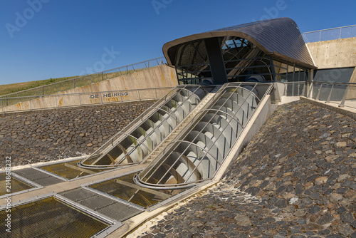 View of the De Heining Archimedes screw pump set into a stone embankment with metal grates and a modern roof structure in Marrum, Friesland, Netherlands.