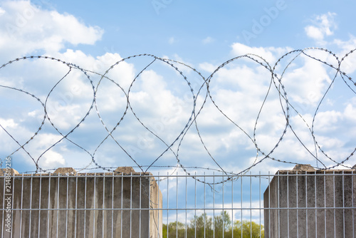 Konstfotografi Razor wire coils forming a secure fence line against a cloudy sky