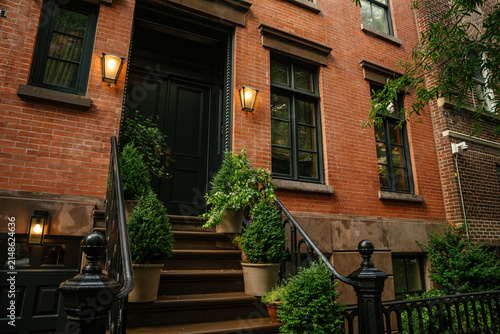 фотографія A traditional New York brick townhouse features a black door and decorative stoop with potted green plants