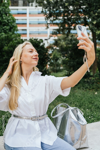 Blonde woman taking selfie with smartphone in park