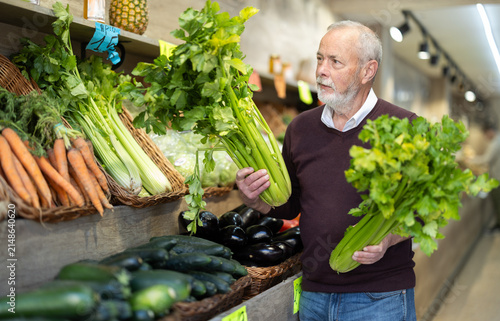 Canvastavla Mature man chooses celery for purchase in greengrocer shop