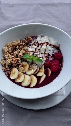 top-down breakfast bowl with sliced banana, granola clusters, coconut flakes, raspberries, mint garnish, and berry base arranged for healthy morning food styling