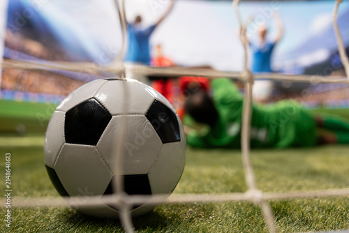 Принти на полотні Close-up of a ball crossing the line and hitting the net as a defeated goalkeeper misses the save, with selective focus framing the ball inside the goal and football players blurred on the pitch