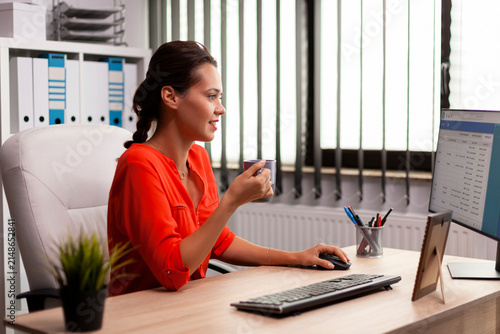 фотографія Corporate entrepreneur remains absorbed in computer work at her office desk, reviewing screen information while managing marketing and business duties