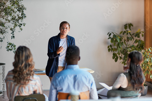 Man presenting to a group of diverse attendees during a business workshop, actively discussing ideas and fostering collaboration in a modern office or educational setting