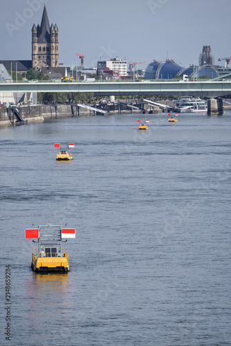 Yellow navigation buoys and fairway markers on the Rhine river in Cologne regulating shipping traffic during extreme low water in front of Severin Bridge