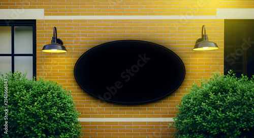 Blank oval sign on a yellow brick wall between two green bushes and two wall lamps, perfect for adding your own custom text or logo for business branding or signage