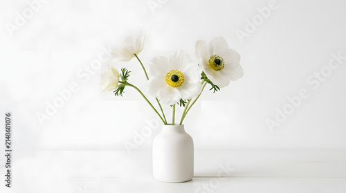 Minimalist white anemone flowers in a small ceramic vase on white surface