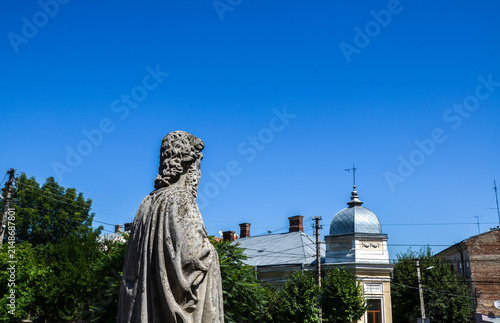 Rear view of the historic stone statue of Apostle Peter in the courtyard of the Armenian Church of Saints Peter and Paul in Chernivtsi, Ukraine, with the architectural details against a blue sky