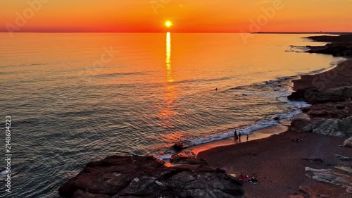 Aerial view of sunset over the ocean with calm waves hitting the sandy beach of the Dune of Pilat where people are walking in Nouvelle-Aquitaine, France.
