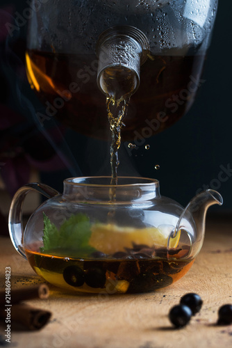Pouring hot herbal tea into a glass teapot with berries and spices