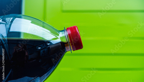 Close Up of Plastic Bottle with Red Cap Against Bright Green Background.