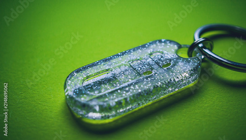 Close Up Metal Key Tag on Green Surface with Dew Drops.