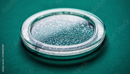 Close Up Glass Lens Case Lid with Water Droplets on Teal Surface.