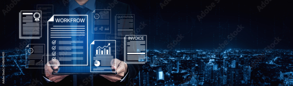 Obraz premium Modern Businessman Holding Digital Tablet with Workflow, Invoice, and Document Graphics Against City Skyline Background at Night. Bitwise.
