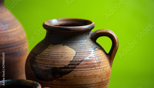 Rustic clay pottery jar with decorative patterns on vibrant green background.