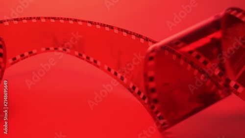 35mm negative photographic film in rotation in red room, camera darkroom. Slightly rolled film strip isolated on red background. Analog film strips. Analog photography. Close-up