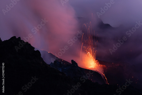 View of Stromboli erupting at night with glowing lava fountains and volcanic ash clouds rising into the dark sky in Lipari, Sicily, Italy.