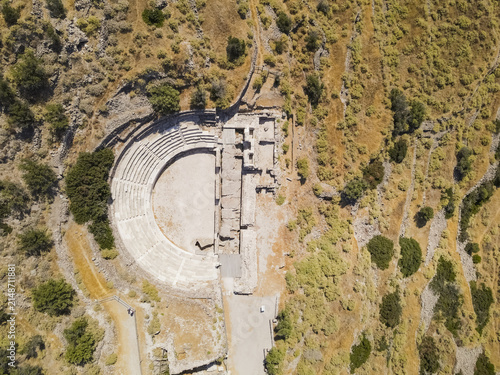 Aerial view of the Ancient Theater of Milos, a well-preserved Roman-era amphitheater nestled in a rugged hillside with stone seating and surrounding dry vegetation in Milos, Greece.