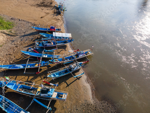 Aerial view of traditional wooden fishing boats moored along the sandy riverbank in Kebumen, Central Java, Indonesia.