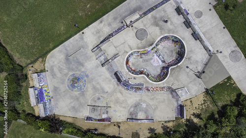 Aerial view of the Bicocca skatepark featuring concrete bowls and ramps covered in colorful graffiti, surrounded by green parkland in Milan, Lombardy, Italy.