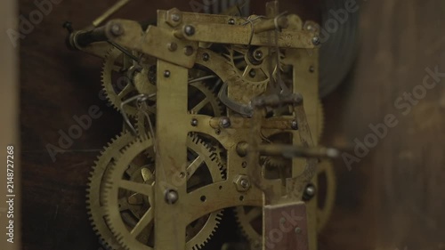 Side view macro shot of layered brass gears, cogs, and wheels spinning inside the internal mechanical movement of a vintage antique grandfather clock.