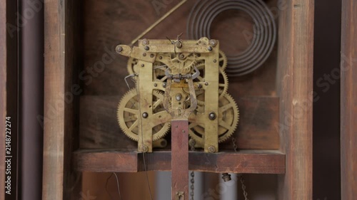 Close up internal shot showing the complex network of brass gears, cogs, wheels, and springs moving inside an antique mechanical grandfather clock.