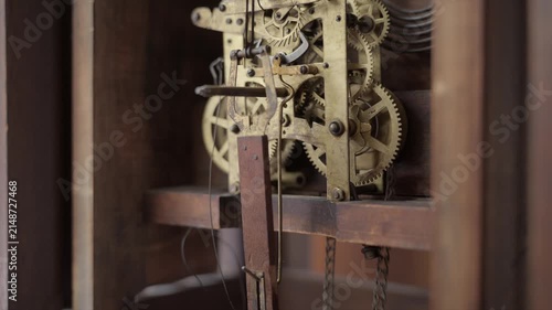 Close up shot of a person pulling a heavy brass weight chain to wind the mechanical gears and internal clockwork of an old antique grandfather clock.