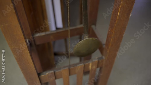 Front view close up shot of a long wooden pendulum with a large round brass disc swinging steadily inside an antique oak Mission style grandfather clock.