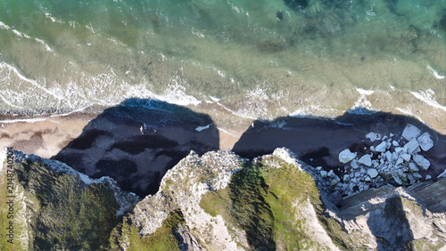 Aerial view of Bulbjerg cliff featuring dramatic limestone formations, rocky debris on the sandy beach, and turquoise sea waves crashing against the shore in Thisted Municipality, Denmark.