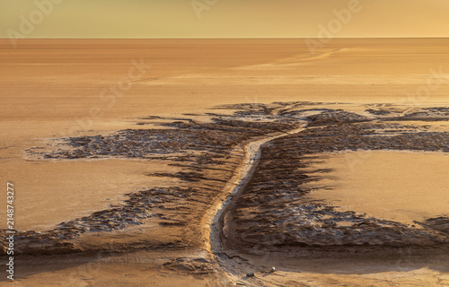 View of the textured salt crust and patterns of Chott el Djerid salt flat under warm golden hour light in Tozeur, Tozeur Governorate, Tunisia.