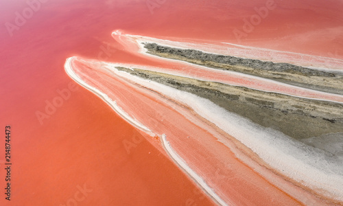Aerial view of vibrant pink salt evaporation ponds with white crystalline shorelines and elongated mineral formations creating an abstract natural composition in France.