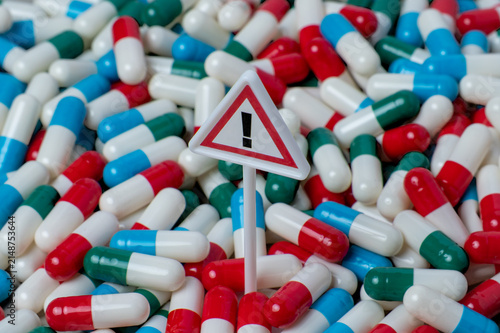 Warning sign standing in a dense pile of colorful capsule pills. Medication risk and side effects, drug overdose concept.