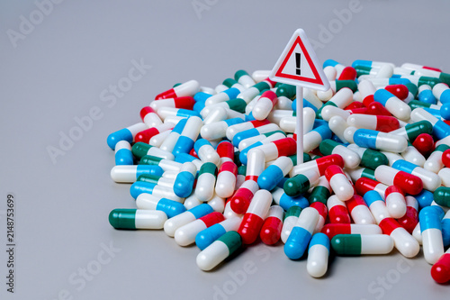 Warning sign standing in a dense pile of colorful capsule pills. Medication risk and side effects, drug overdose concept.