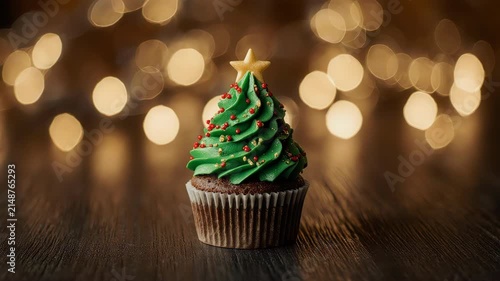 Close-up Christmas tree cupcake on rustic wooden surface, green frosting swirl with tiny sugar decorations, pinecones and red ornaments 