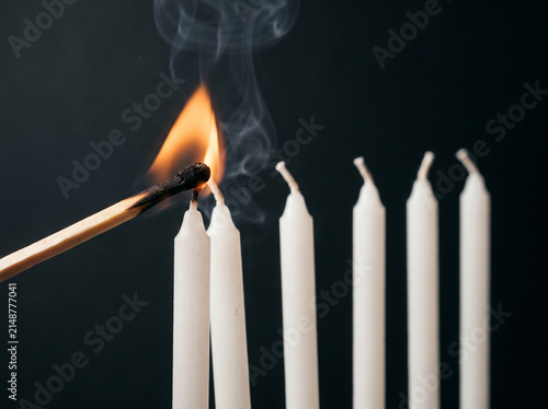 One lit match reaching to relight a row of extinguished candles