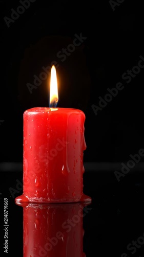 Burning Red Pillar Candle With Melting Wax Dripping on Reflective Surface