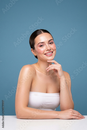 Smiling Young Woman with Hand on Chin Against Blue Background
