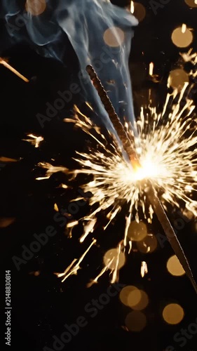 Bright Sparkler Burning With Golden Sparks and Smoke Against Dark Background With Bokeh Lights