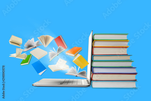 Books are stacked beside a laptop with pages flying up