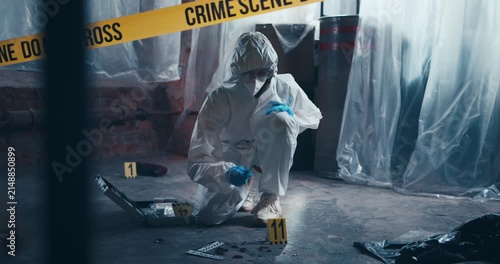 Crime scene specialist in protective clothing inspects trace evidence on the floor during a forensic investigation.