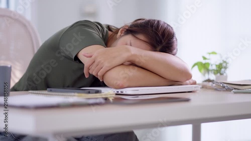 Exhausted Asian woman experiencing burnout resting head on desk during remote work at home office with copy space