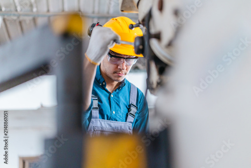 Factory worker operating industrial drilling machine to machine metal part in workshop
