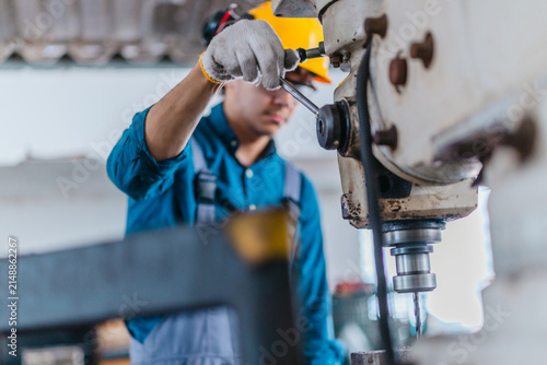 Factory worker operating industrial drilling machine to machine metal part in workshop